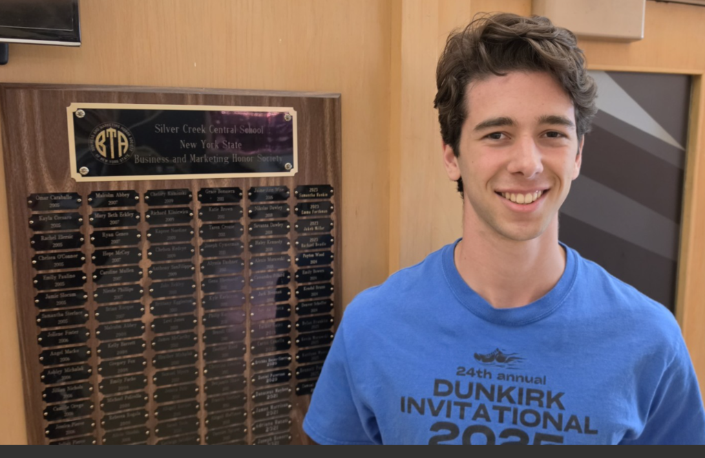 Sam Bowers standing by plaque in lobby