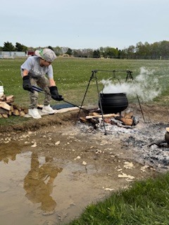 student stoking fire under cooking pot