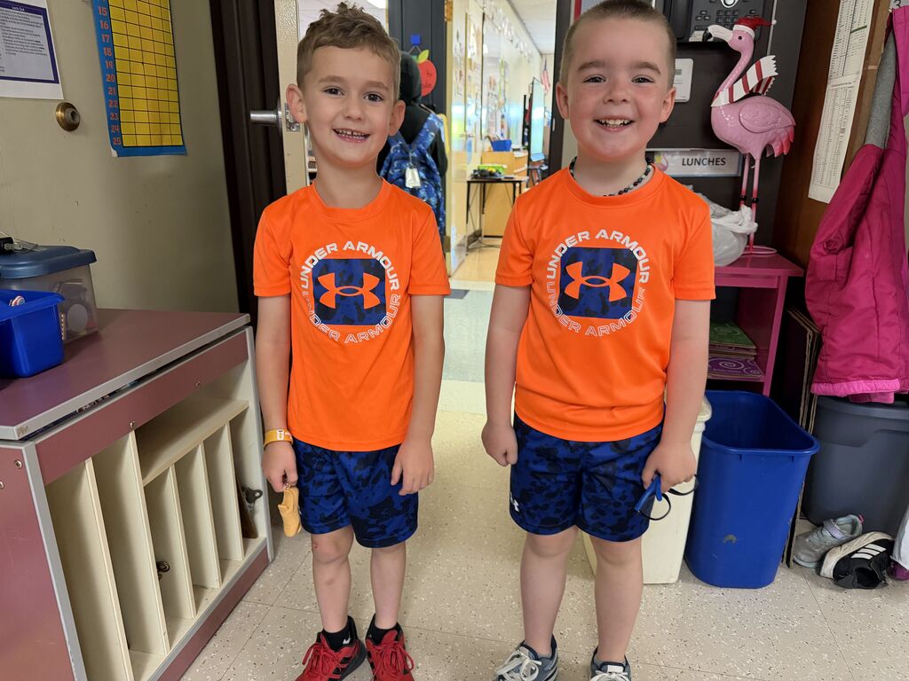 Two elementary students wear orange shirts and blue shorts. 