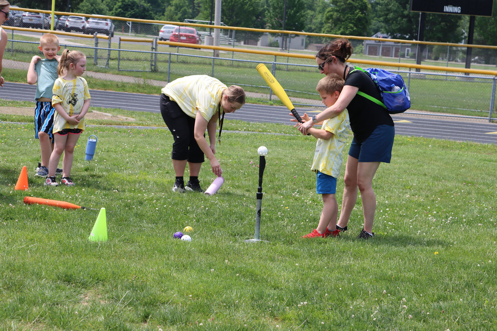 A teacher shows a student how to swing a bat for tee ball. 