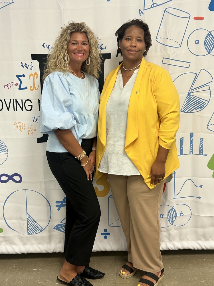 Mrs. Stacy Cockrell and Mrs. Kristy Thurman pose for a photo in front of a math themed backdrop.