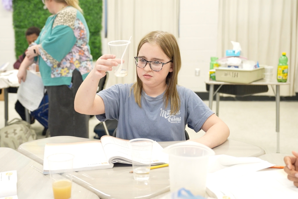 Student is holding up a cup with a liquid and is examining it for their lesson on mixtures and solutions. 