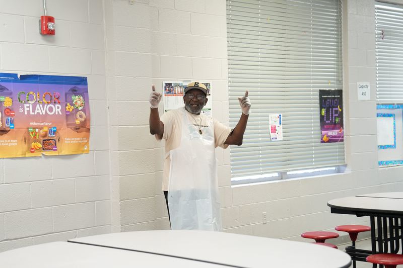 A cafeteria worker is posing for a picture inside Magee High School's cafeteria