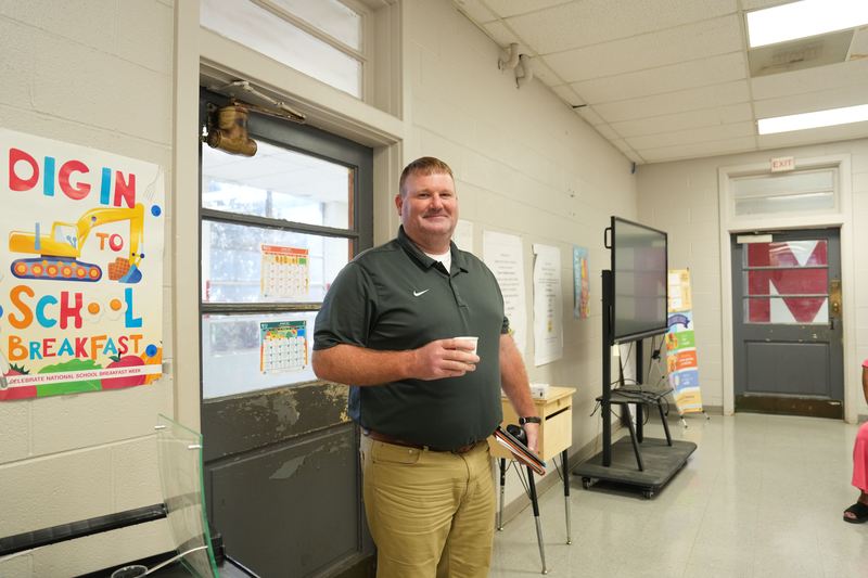 A coach is posing with a cup of Moo Brew coffee