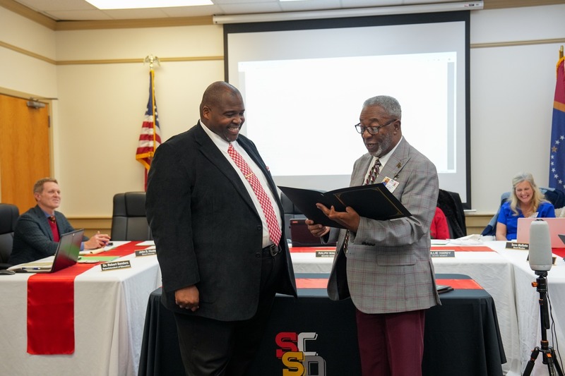 Board president presents a  resolution to the superintendent.