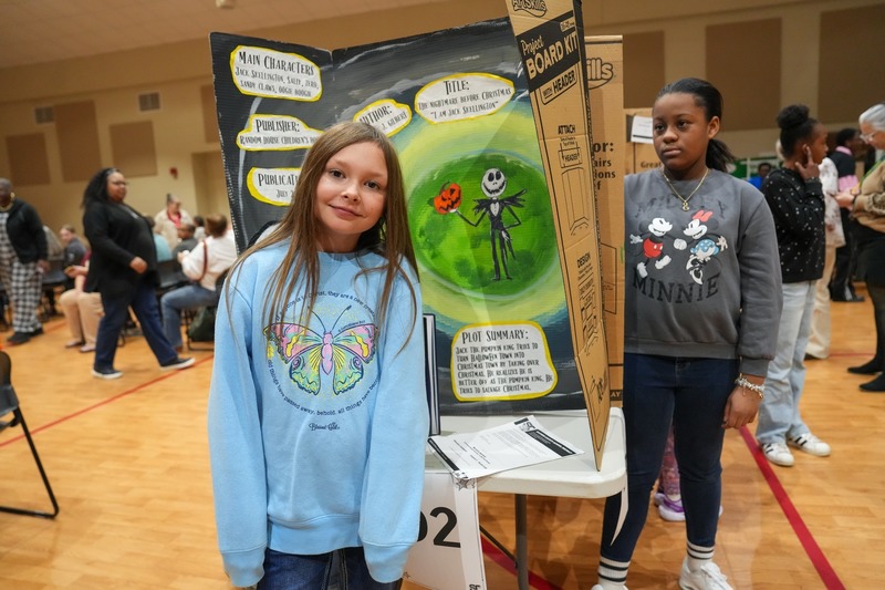 Students standing near their reading fair projects.