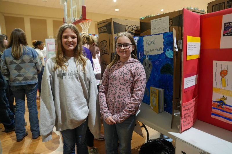 Students standing near their reading fair projects.
