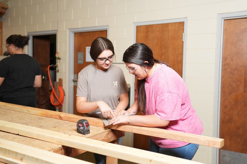 Two students are measuring wood