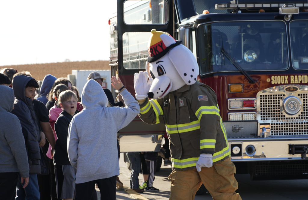 student high fives Sparky for fire prevention week.