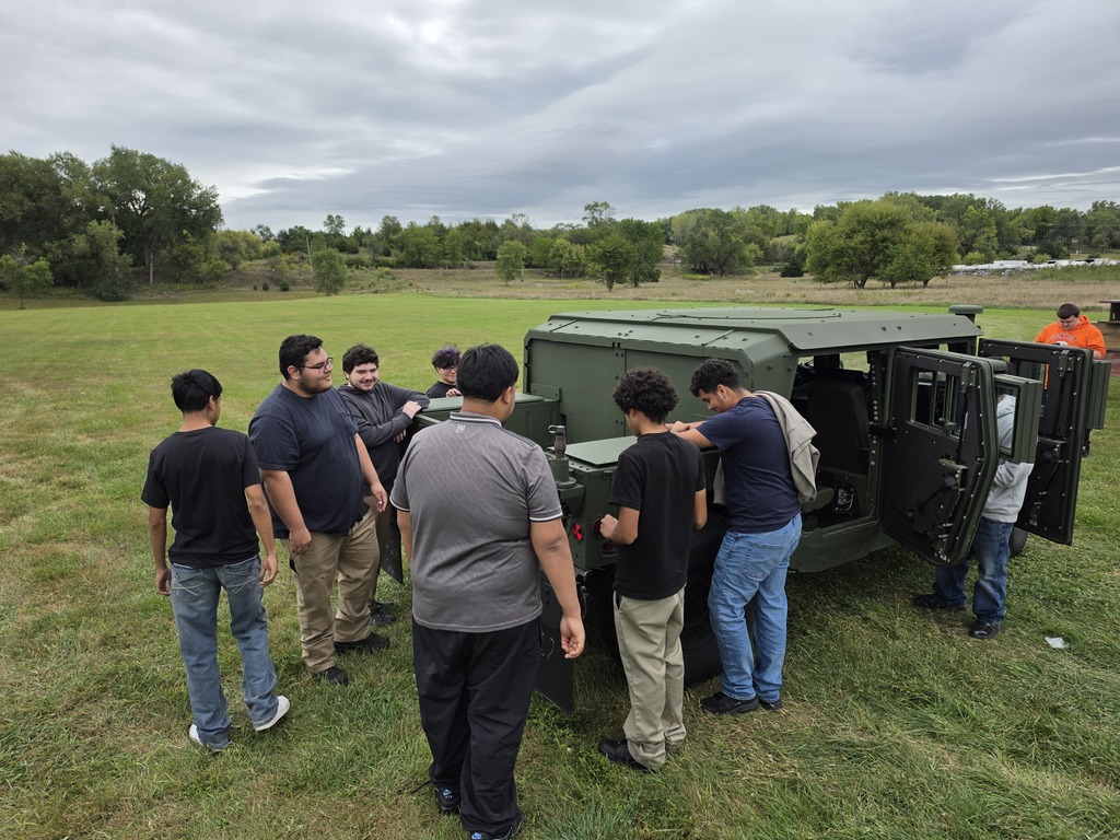 Harry Hopkins Career Academy students gather around and explore a military vehicle during a National Guard visit. Several students are looking inside the vehicle and examining its exterior while standing on a grassy field.