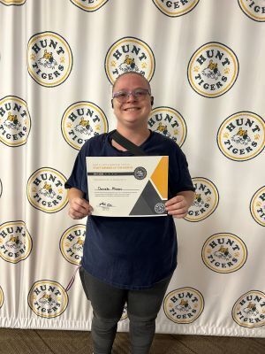 woman with glasses holds a certificate in front of a white backdrop