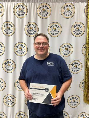 man with glasses holds a certificate in front of a white backdrop
