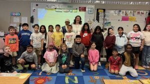 class of children and their teacher stand in front of a white board while smiling