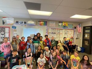 class of children and their teacher stand in front of a white board while smiling