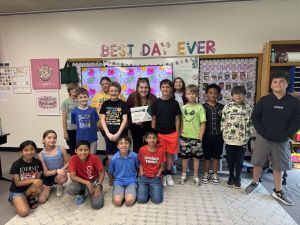 class of children and their teacher stand in front of a white board while smiling