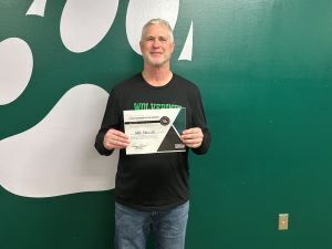 man with gray hair holds a certificate in front of a green wall
