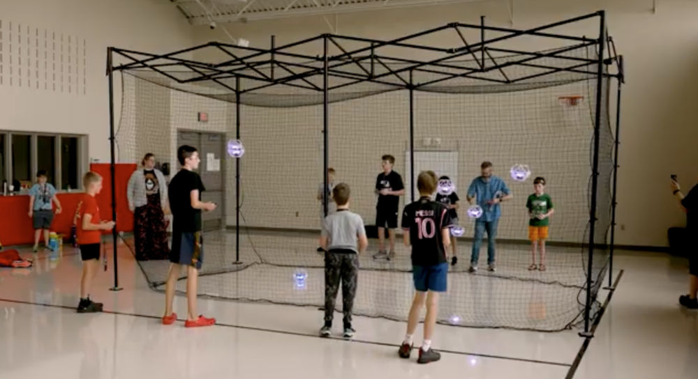 Middle school students stand alongside a square net with game controllers flying drones as part of SFSD's newest esport, drone soccer!