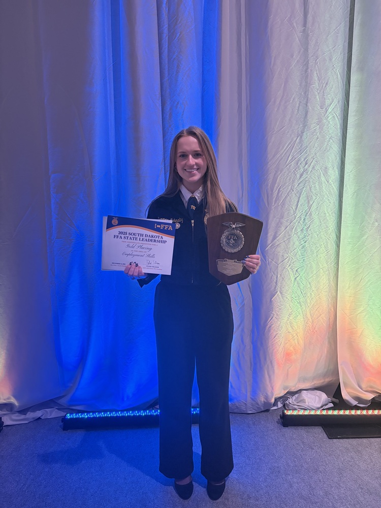 A student holds up a letter and plaque displaying her award in FFA competition