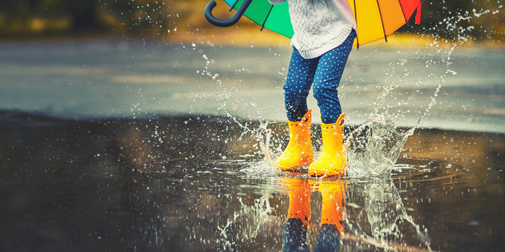 Child wearing rain boots splashing in a puddle. 