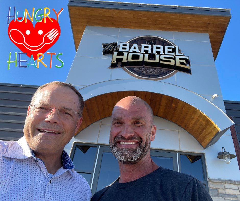 Two men stand in front of the barrel house restaurant smiling