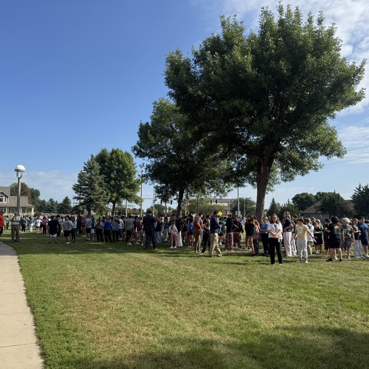 Students from Memorial Middle School gather outside the building during a fire drill. They are standing in organized lines on the sidewalk with staff nearby, demonstrating safe and calm behavior. 