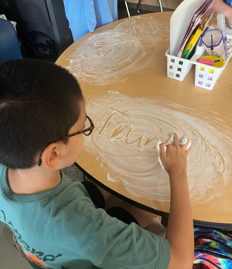 5th graders working on guided spelling using shaving cream on a table. 
