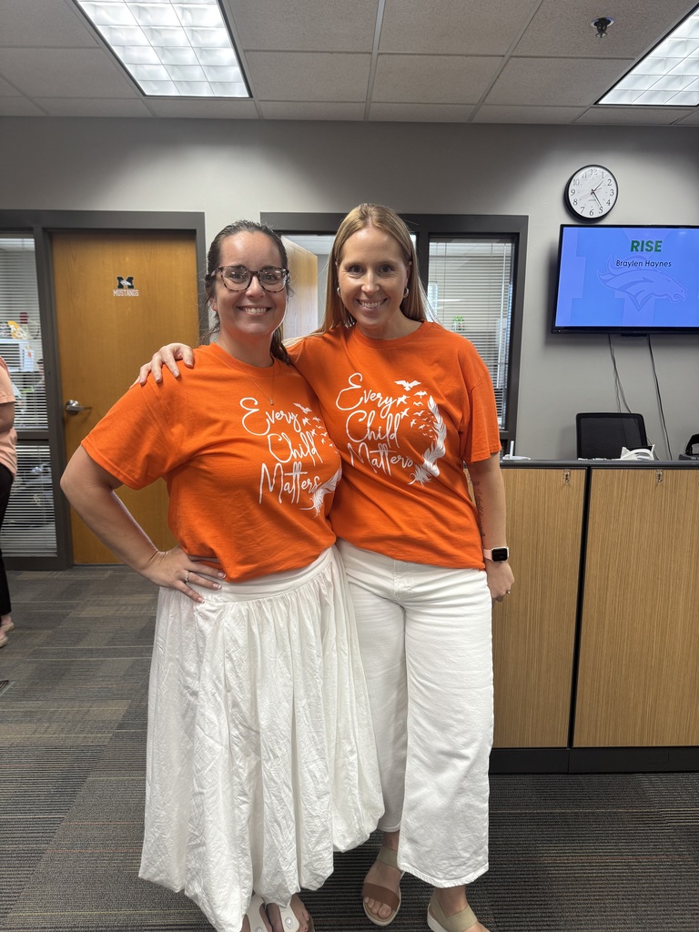 A close-up shot of two women in orange t-shirts with the words "Every Child Matters" printed in a white, decorative font.