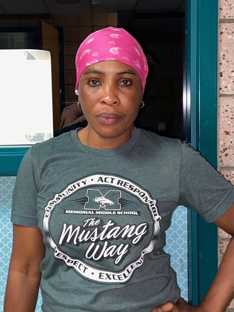 Staff member wearing a pink bandana and a green “Memorial Middle School • The Mustang Way” T-shirt stands in a school hallway, facing the camera.