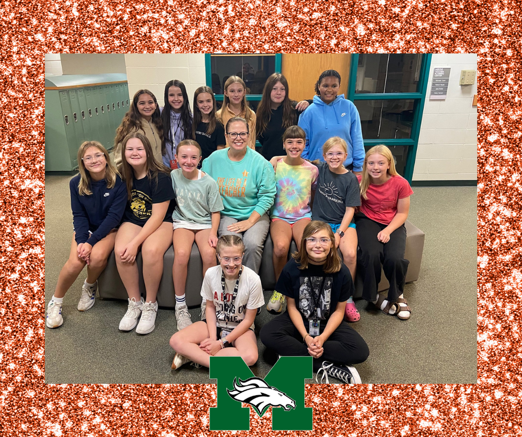 Mrs. Hansen, a teacher, is gathered with a group of smiling middle school students in their team area to celebrate a new Taylor Swift album release.