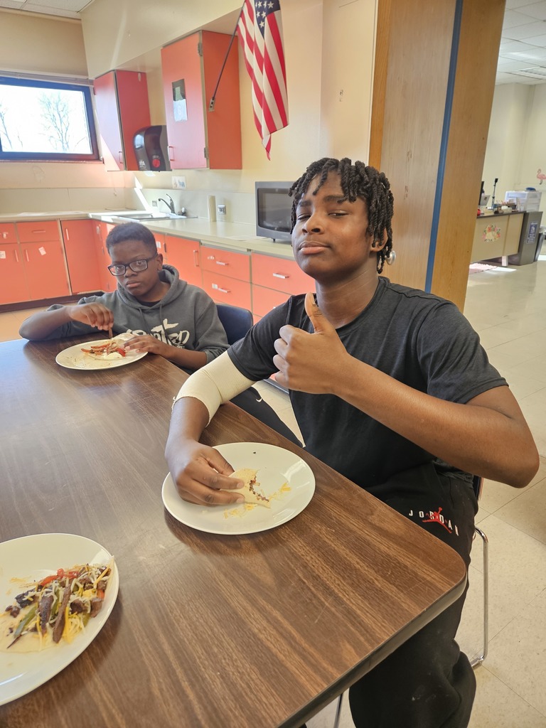 Two boys sitting at a table giving a thumbs up