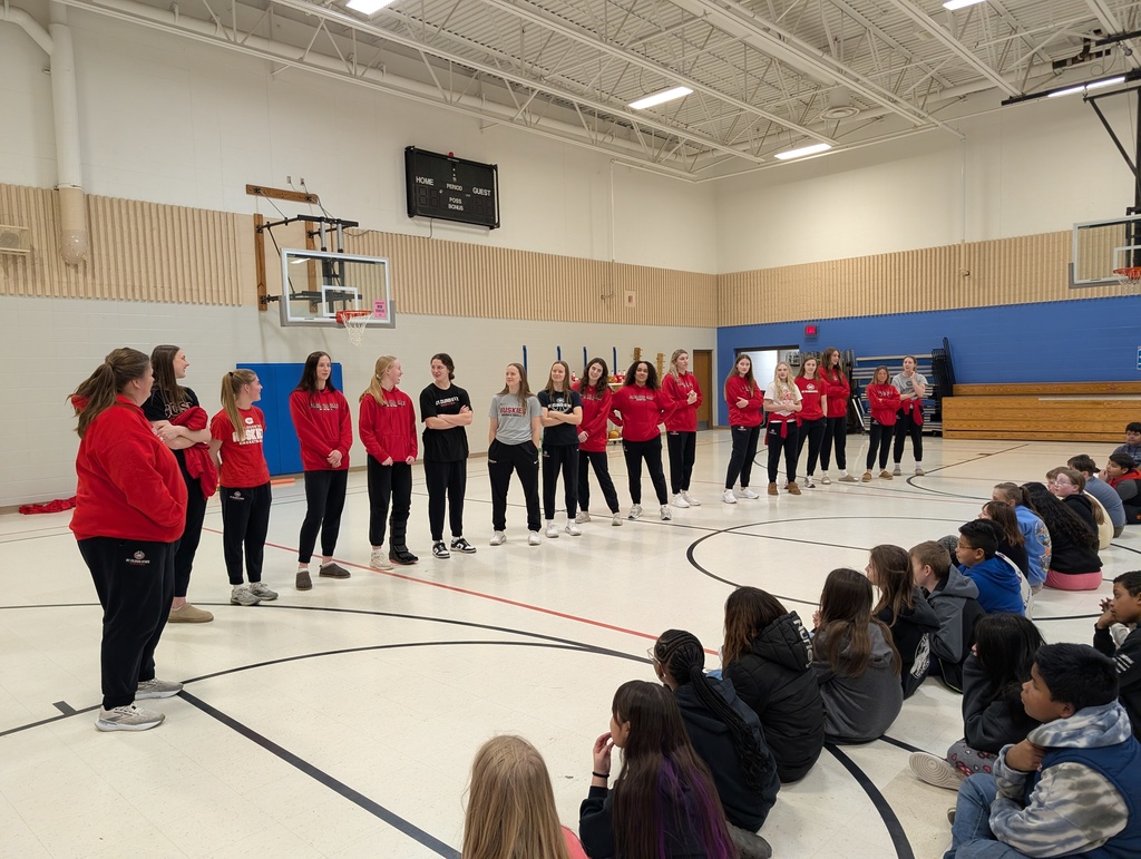 SCSU Women's basketball team standing before students in elementary gym.