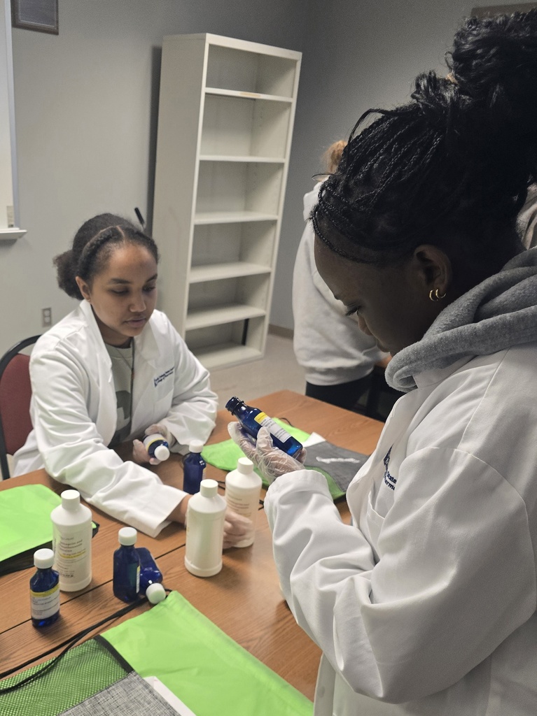 Two students in white lab coats looking at blue glass bottles.