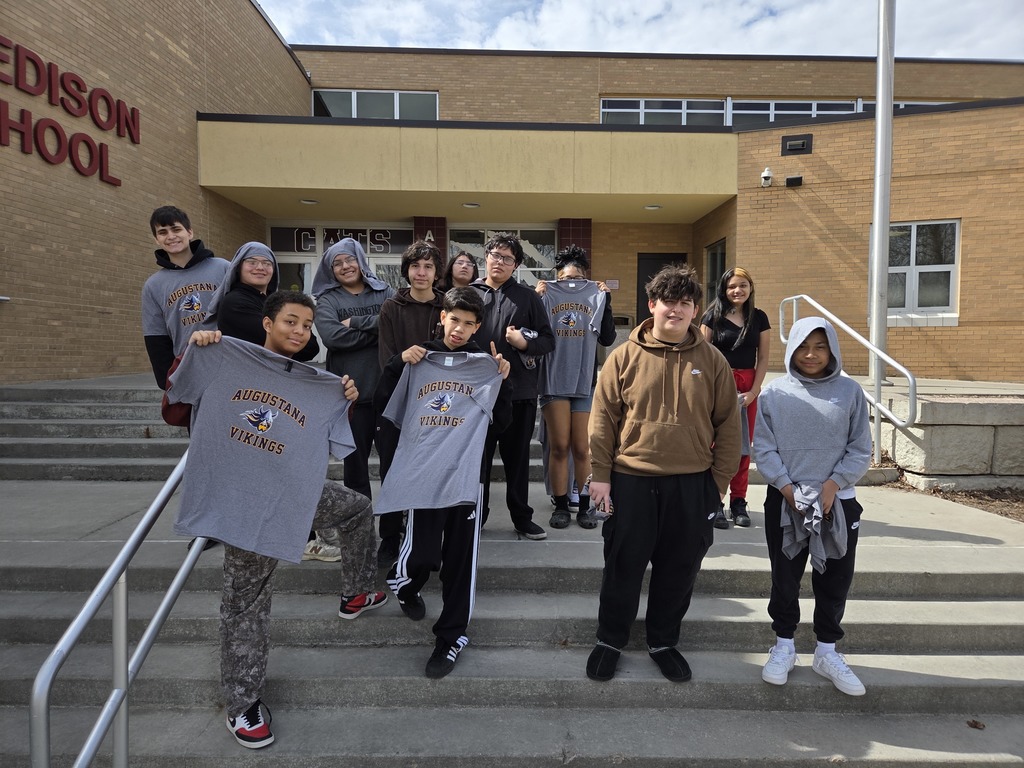 students standing on the front steps of edison middle school. many are holding augustana university shirts and smiling while a few students are wearing their shirts on their heads and posed together 