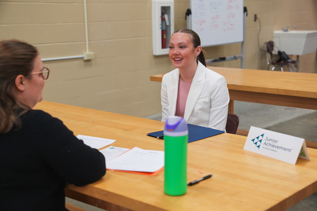 Academy of Finance student sits confidently at a table making eye contact and smiling at the Junior Achievement representative during a mock interview at the CTE Academy.