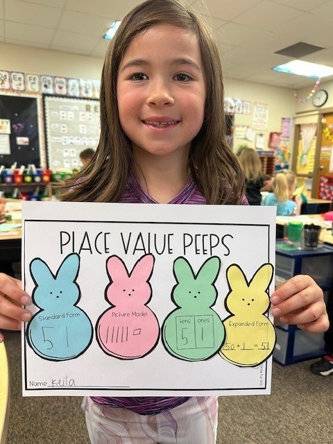 student holding up place value paster with peeps