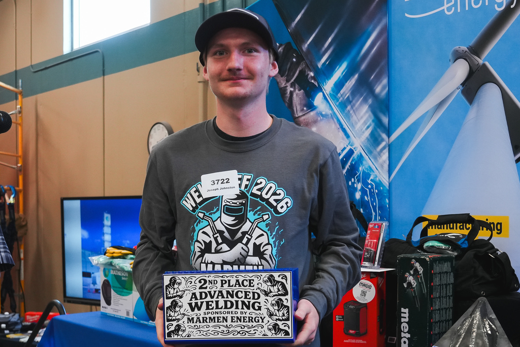 A young man holds a trophy that says 2nd place advanced welding sponsered by marmen energy on it