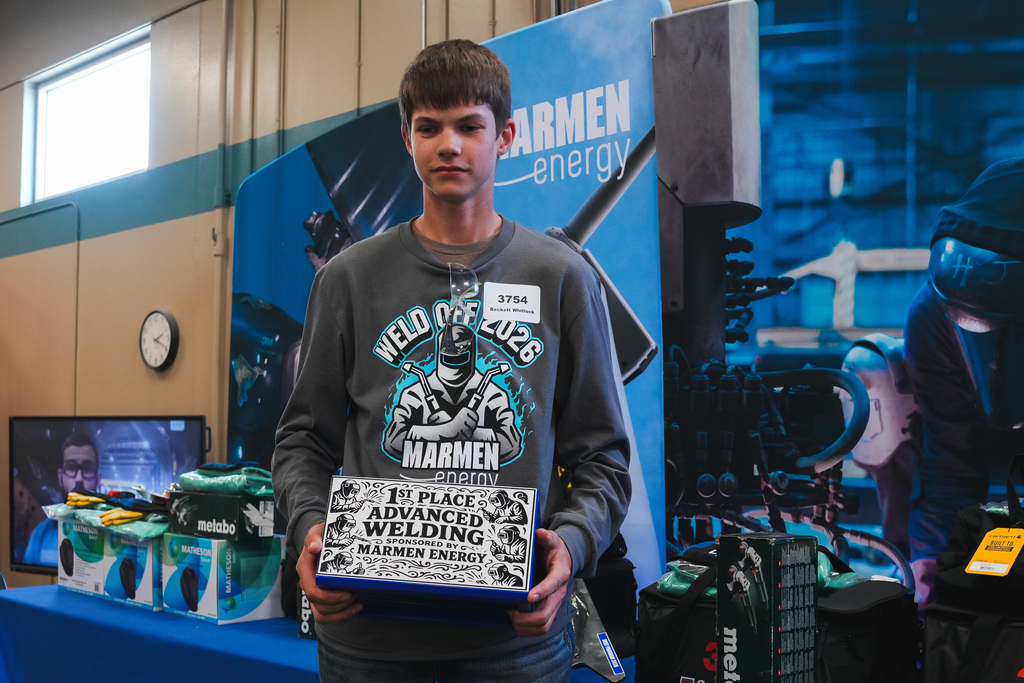 Beckot Whitlock holds a first place in advanced welding award wearing a shirt that says Weld Off 2026 in front of a sign that says says Marmen Energy.