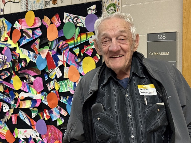 a man in a black shirt and black jacket standing in front of a colorful background 