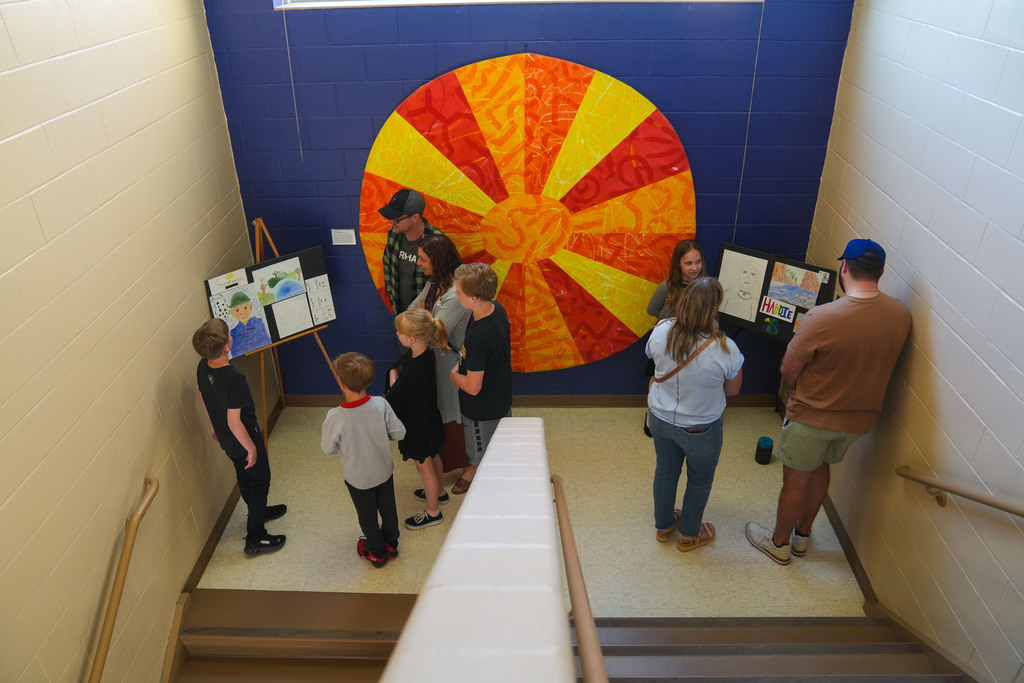 Kids talk to adults in a stairwell explaining their works of art which stand on easels