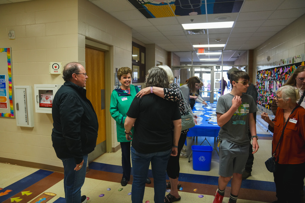 Two woman share a hug while talking to another man and a woman. An older woman talks to a young boy on the side. 