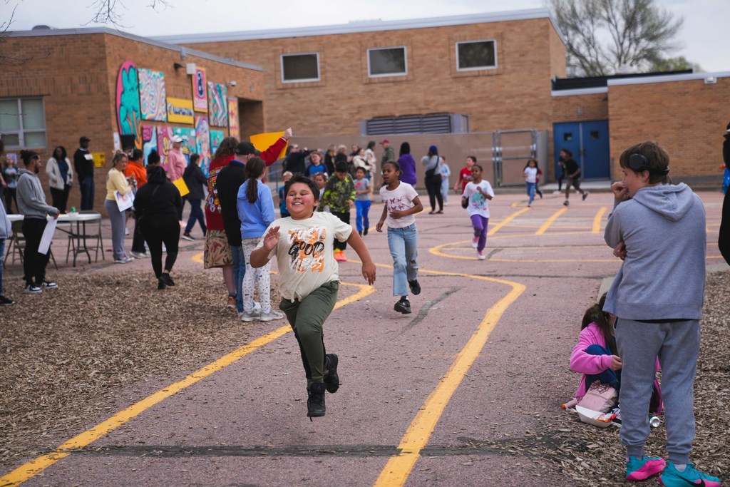 A young boy runs on the school playground as a group of other students follows behind him in a foot race