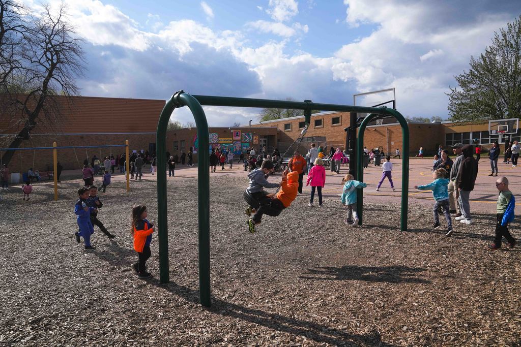 Kids swing on a tire swing on a school playground as a group of kids plays around them