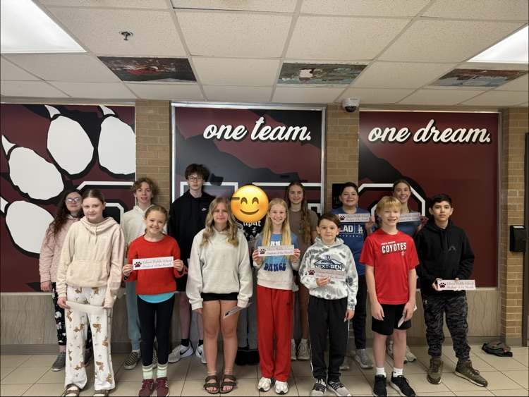 A group of Edison Middle School students stand together in a school hallway smiling for a photo while wearing Student of the Month stickers.
