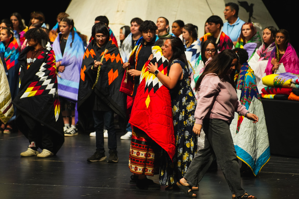 A mom hugs her student wrapped in a traditional Star Quilt on the stage of the Washington Pavilion during SFSD's Annual Native American Honoring Ceremony on Monday, May 11