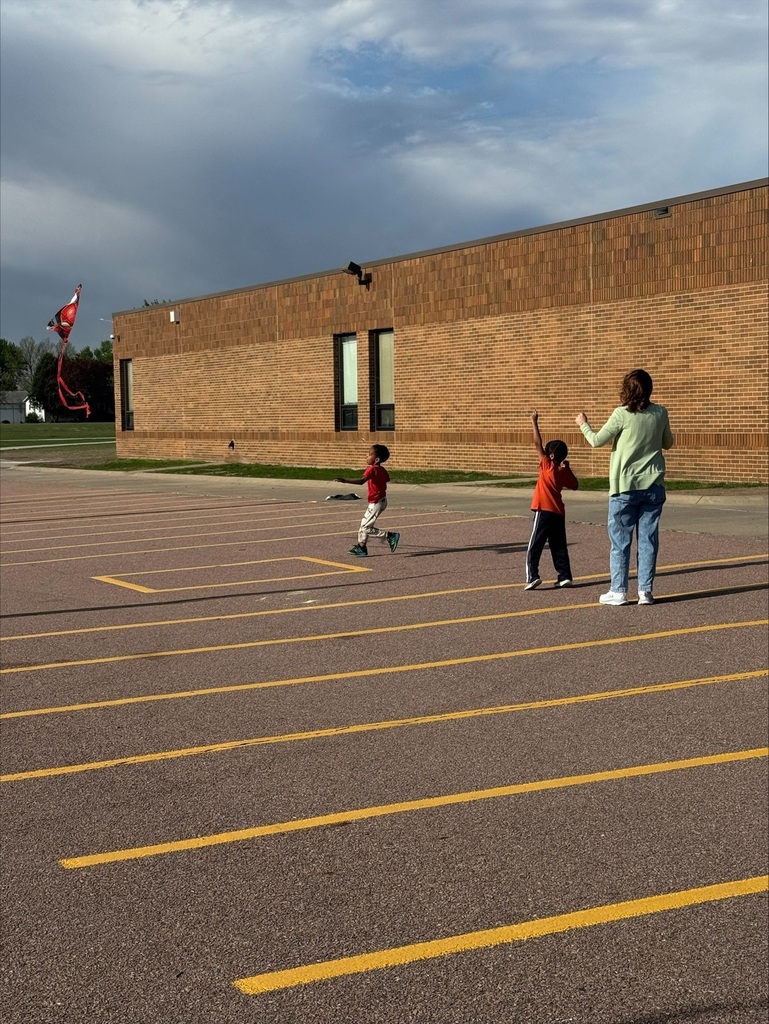 children flying kites on the school playground with teacher