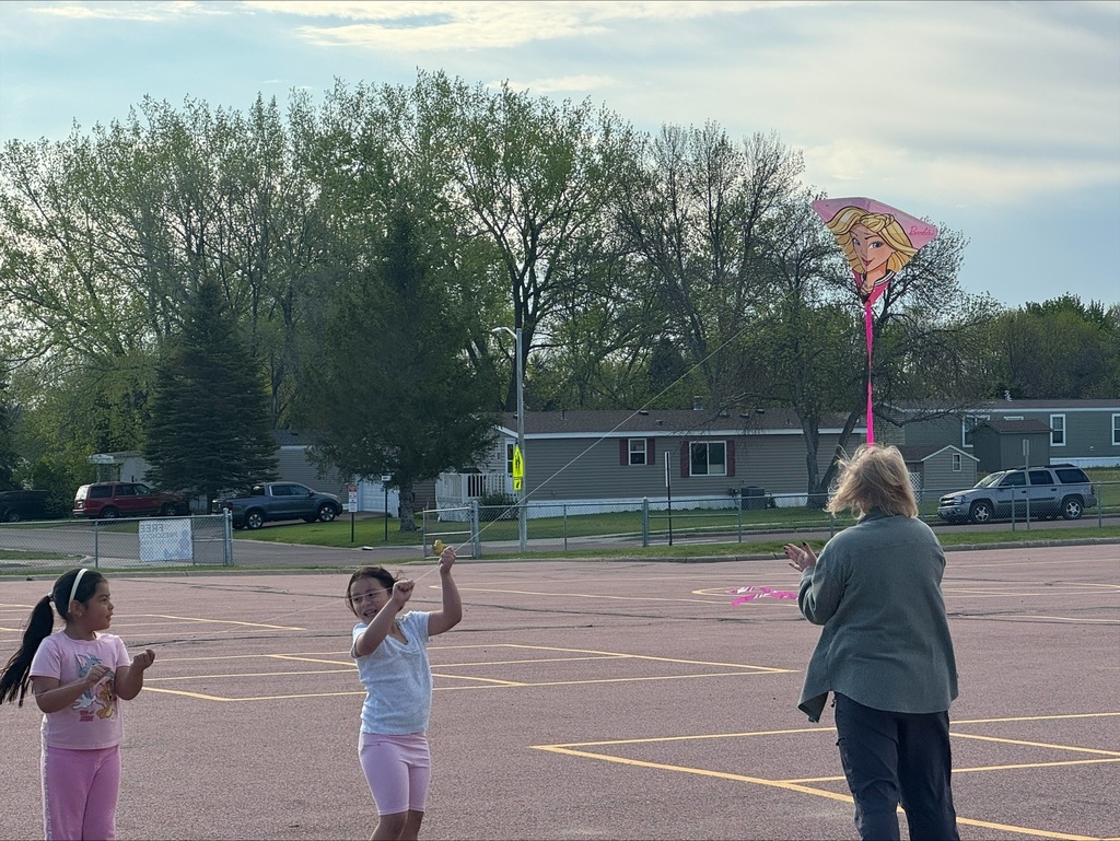children flying kites on the school playground with a teacher