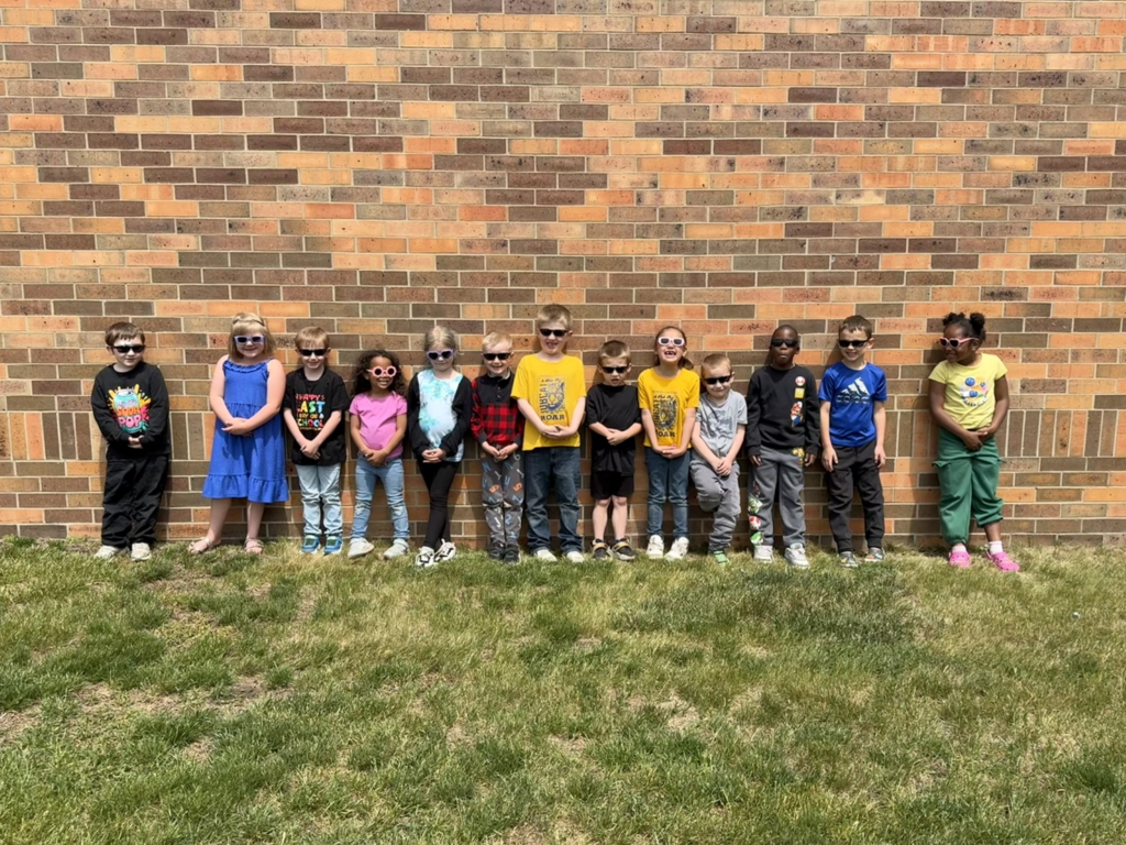 kindergarten students standing by the wall outside with sunglasses on