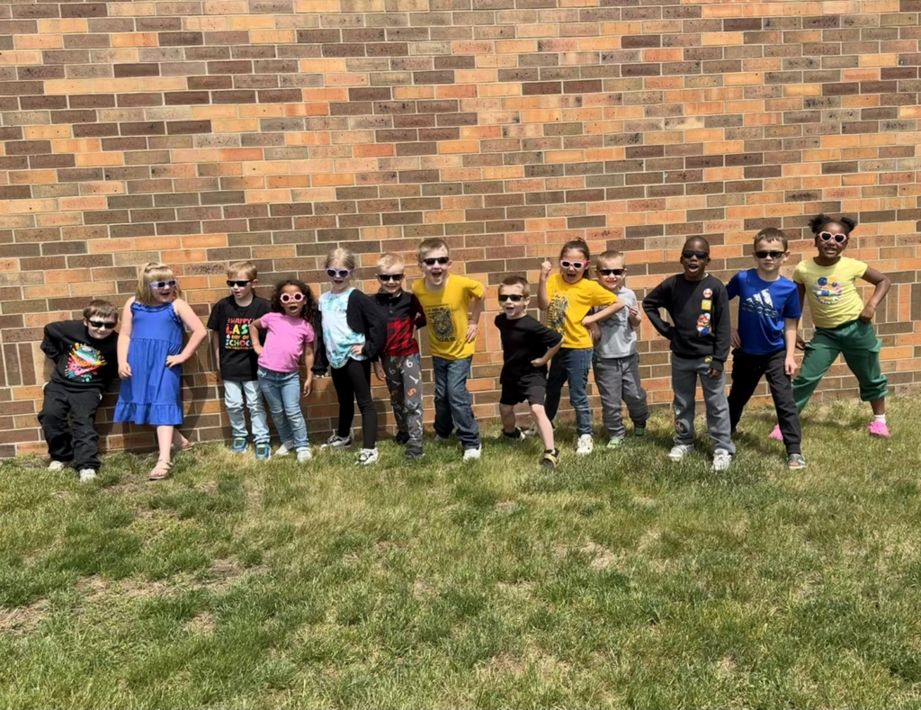 kindergarten students standing by the wall outside with sunglasses on