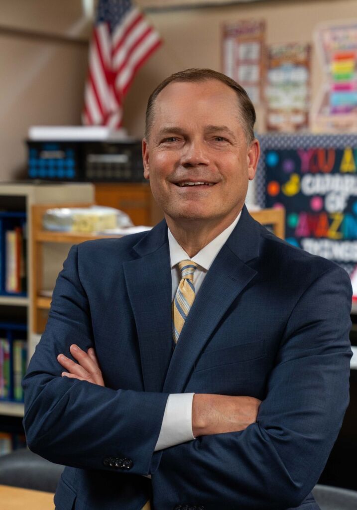 Superintendent Dr. Jamie Nold standing in an elementary school classroom with his arms folded, smiling. 