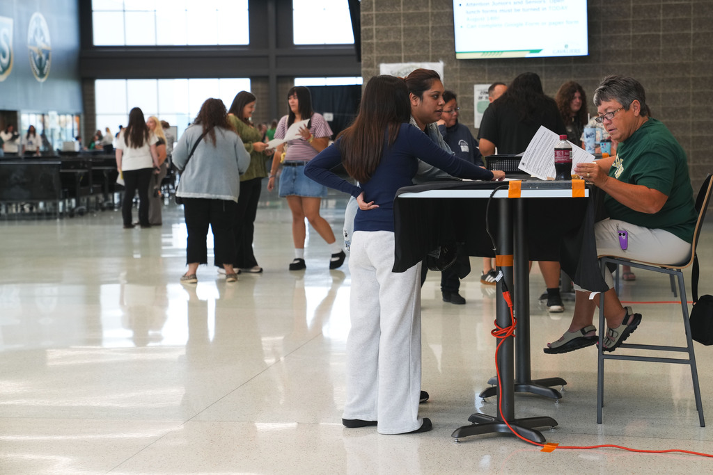 A JHS teacher sits behind a table in the commons area looking at a sheet of paper while helping students during Cavalier Day on Friday, August 14, 2026. 